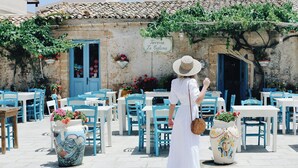 A woman in a white dress and hat walking past a building with a sign reading "Taverna La Ciuola".