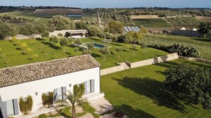 A villa with a swimming pool, surrounded by well-maintained gardens and fields.
