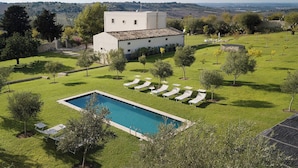 A pool area with lounge chairs, a white building, and a view of the countryside.