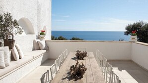 A terrace with a view of the sea, a wooden table with chairs, and a white wall with a plant. - Blu Melia - Seven Bedroom Villa, Sleeps 14 (Contrada Guardiola)