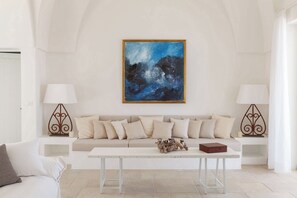 A modern living room with a white sofa, two side tables with lamps, a white coffee table, and a large abstract painting on the wall.