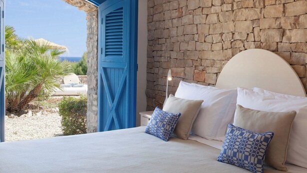 A bedroom with a stone wall, a bed with white linens, and a view of the sea through an open archway. - Blu Melia - Seven Bedroom Villa, Sleeps 14 (Contrada Guardiola)
