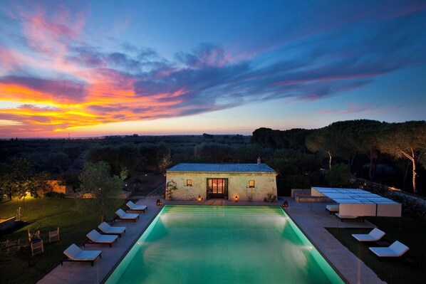 Un espace piscine avec des chaises longues, un petit bâtiment doté d’une porte et une vue sur le coucher de soleil.