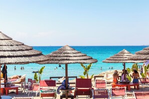 Une plage avec des parasols en chaume et des chaises longues rouges.