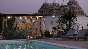 A stone building with conical roofs, a pool, and lounge chairs.