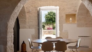 A dining area with a stone arch, a table with chairs, and a view of a tree and garden through a window.