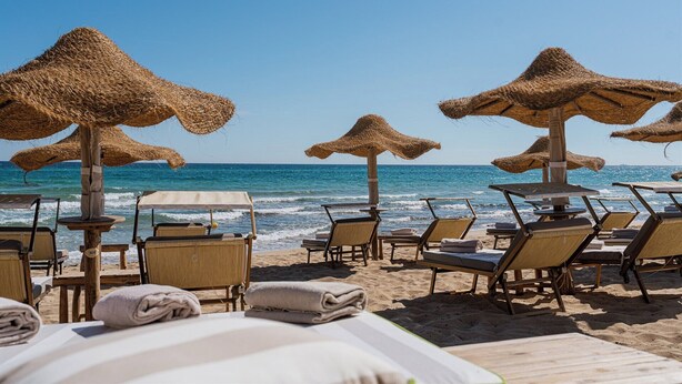 A beachside hotel with thatched umbrellas, sun loungers, and wooden tables.