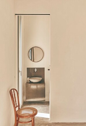 Un baño con un espejo redondo, un lavamanos y una silla.