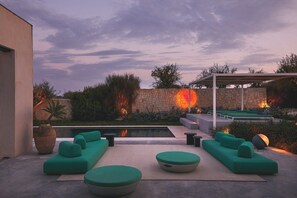 Un patio moderno al aire libre con piscina, mobiliario verde y una pared de piedra.