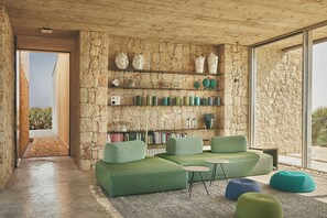 Un intérieur moderne avec un mur en pierre, des sièges recouverts d’un tissu vert et une vue à travers une porte vitrée.