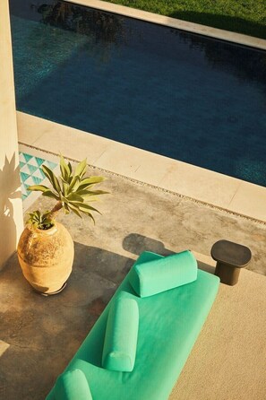 Zona junto a la piscina con un sillón de descanso, una planta en maceta y suelo de baldosas.