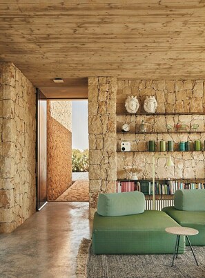 Un interior moderno con una pared de piedra, asientos tapizados en verde y una estantería.