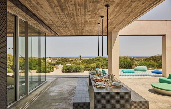 Un espacio moderno para comer al aire libre con vista al mar, techo de hormigón y diseño minimalista.