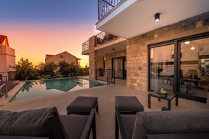 Un espace piscine extérieur moderne, doté de chaises longues, d’un mur en pierre et d’une porte vitrée donnant sur un balcon.
