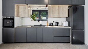 Una cocina moderna con armarios oscuros, horno empotrado, refrigerador de acero inoxidable y ventana con vistas a la vegetación.
