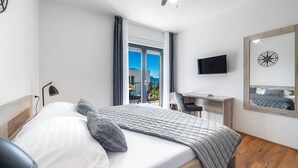 Un dormitorio con cama, escritorio, silla, televisor y ventana con cortinas.