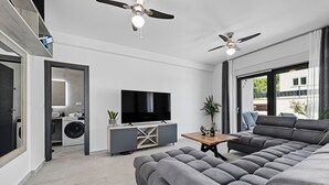 Una sala de estar moderna con un sofá seccional gris, un televisor de pantalla plana, una mesa de centro de madera y ventiladores de techo.