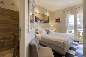 Un dormitorio con cama, una silla, un baño con bañera y vistas al mar.
