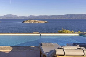 Zona de piscina con sillones de descanso y vistas al mar y las montañas.
