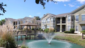 A residential building with a central courtyard featuring a fountain, surrounded by manicured lawns and a wooden bridge. - Legacy Villa 1701 | Just a Short Walk to the Beach! (Gulfport)