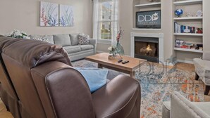 A living room with a leather sofa, a grey sofa, a coffee table, and a fireplace. There are bookshelves and a globe on the wall. - Legacy Villa 1701 | Just a Short Walk to the Beach! (Gulfport)