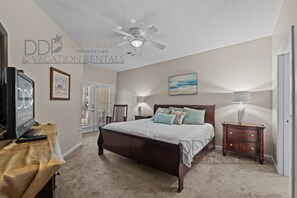 A bedroom with a bed, a ceiling fan, a TV, and a lamp.