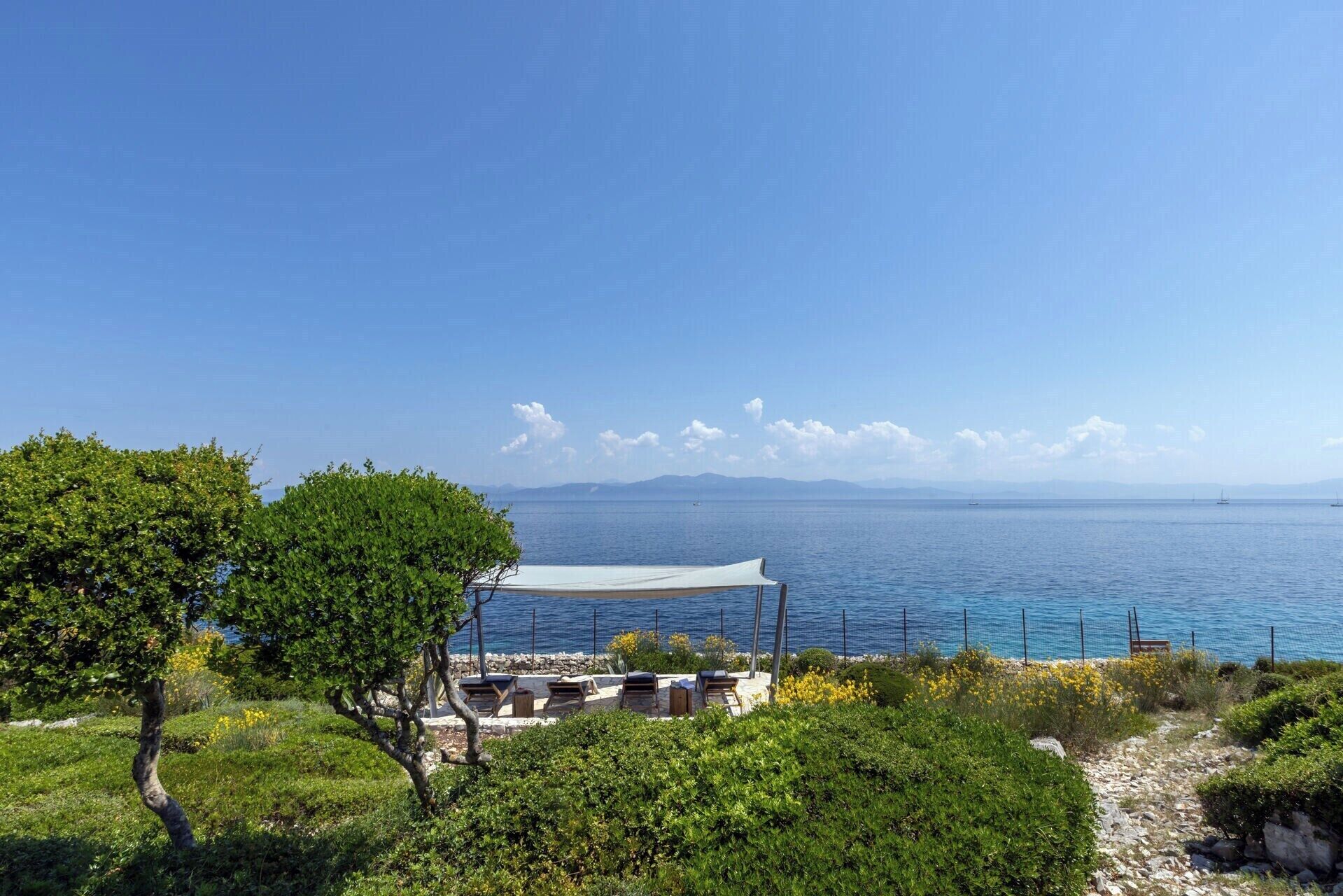 A coastal view with a seating area, a covered structure, and a clear sky.