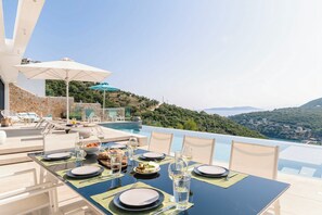 Mesa de jantar posta para seis pessoas, com vista para o mar e colinas.