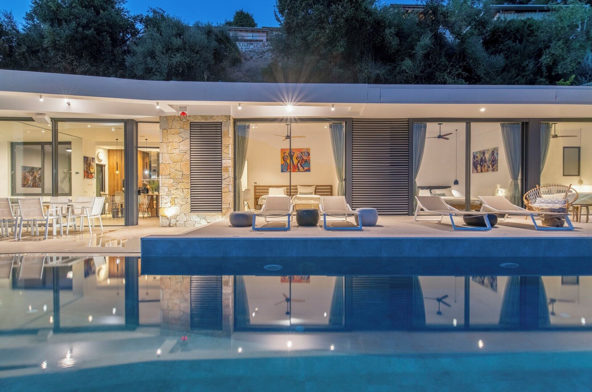 A modern poolside area with lounge chairs, a dining area, and a bedroom with a large window.