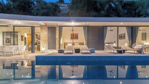 A modern poolside area with lounge chairs, a dining area, and a bedroom with a large window.
