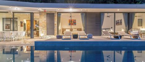 A modern poolside area with lounge chairs, a dining area, and a bedroom with a large window.