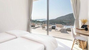 A bedroom with a large sliding glass door leading to a terrace with outdoor seating and a scenic view.