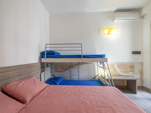 Habitación con literas, cabecera de madera, escritorio e iluminación en la pared.