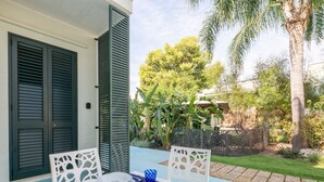Zona pranzo all'aperto con tavolo apparecchiato per due, sedie bianche e tovaglia blu.