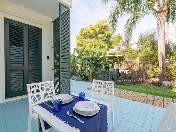 An outdoor dining area with a table set for two, white chairs, and a blue tablecloth.