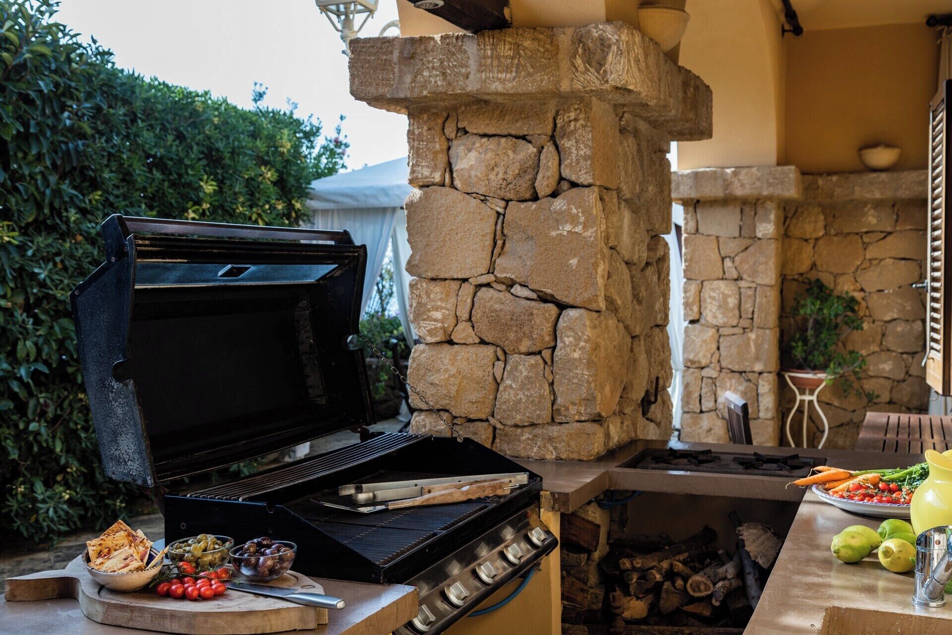 An outdoor kitchen with a stone chimney, a grill, and a variety of food items.
