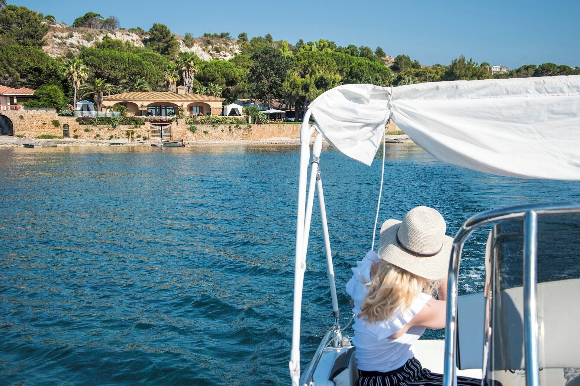 A boat with a white canopy, a person wearing a hat, and a coastal landscape with buildings in the background.