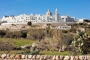 Um edifício branco com um campanário, cercado por vegetação e uma parede de pedra.