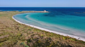 A coastal landscape with a sandy beach, clear turquoise waters, and a small island with a structure.