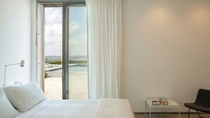 A hotel room with a bed, a small table with bowls, a chair, and a view of a cityscape through a large window. - Dietro al Muro - Four Bedroom Villa, Sleeps 10 (Avola)