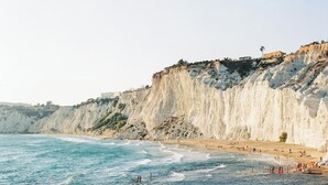 Escena costera con acantilados, una playa y un edificio sobre los riscos.