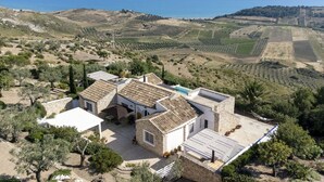 Una villa con techo de tejas anaranjadas, rodeada de olivares y vistas al mar.