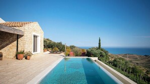 Una piscina con vistas despejadas al mar, un edificio de piedra y plantas en macetas.