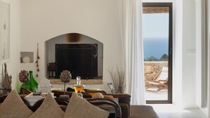 A living room with a fireplace, a view of the sea, and a dining area with a table and chairs.