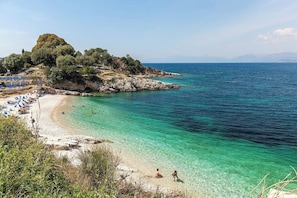 A beach with clear turquoise water, a rocky outcrop with trees, and a row of beach umbrellas. - Khaleesi - Four Bedroom Villa, Sleeps 8 (Ionian Islands)
