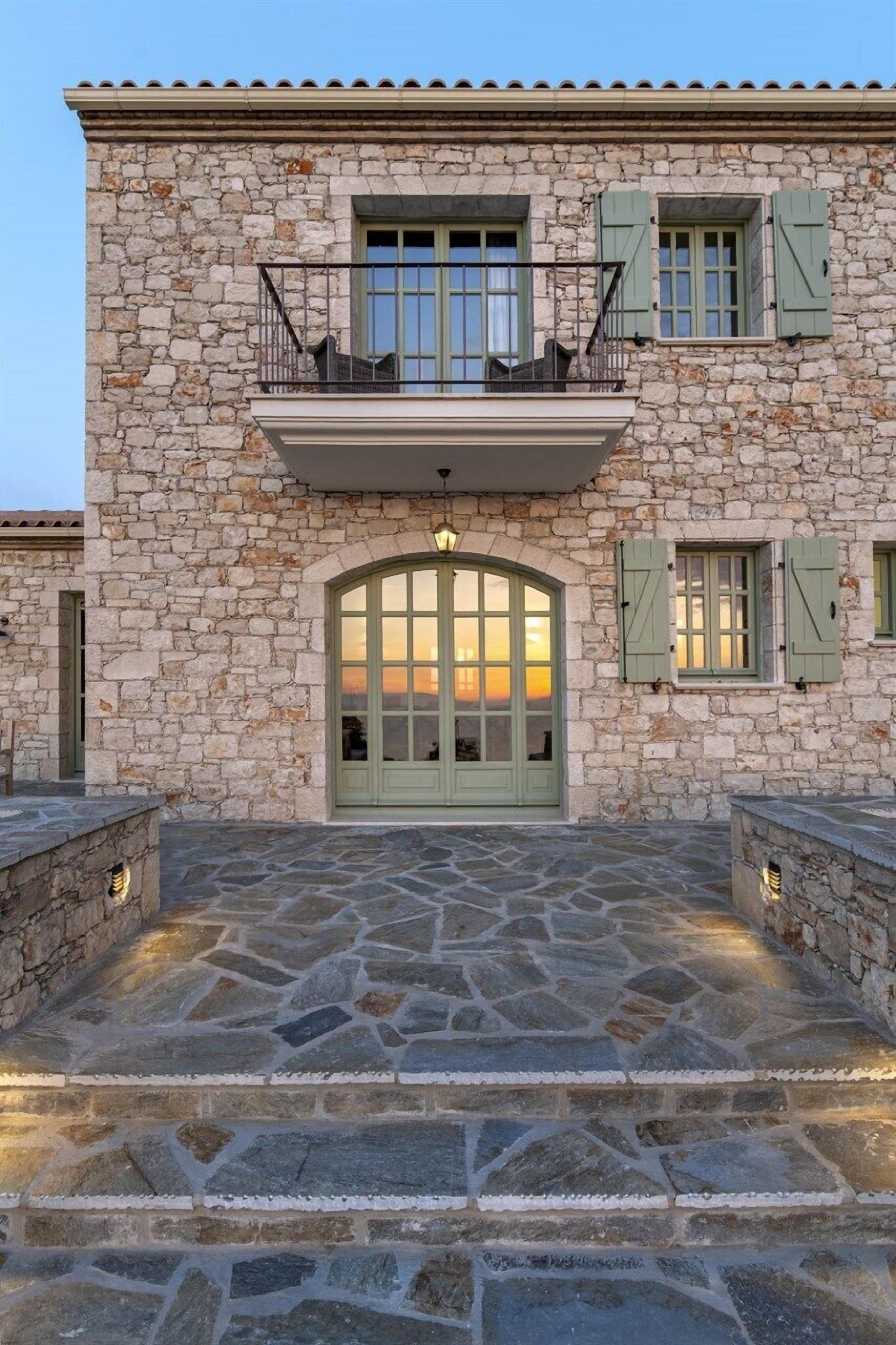 A stone building with a large arched entrance, green shutters, and a balcony.