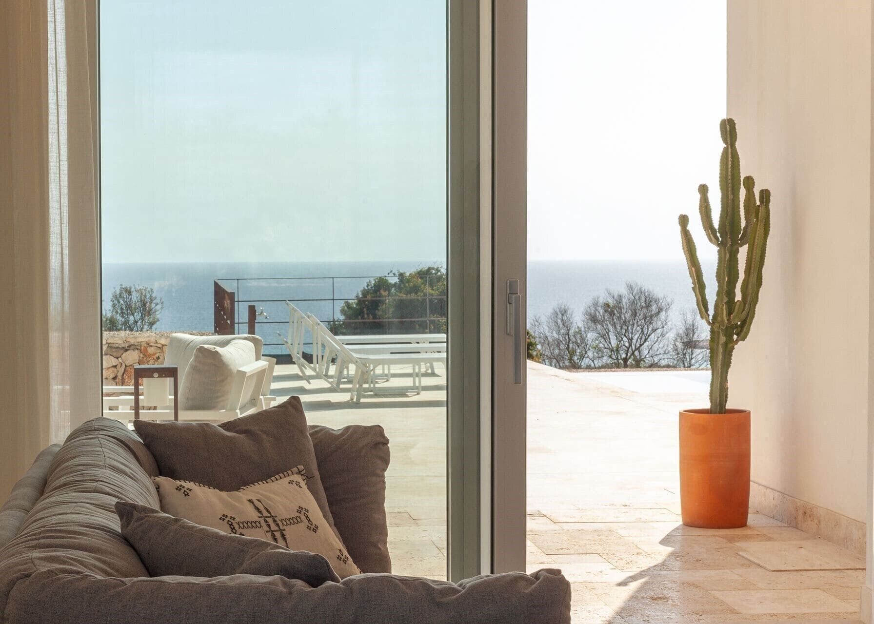 A room with a large sliding glass door leading to a balcony with a view of the sea.