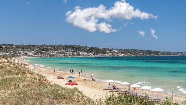 A beach with clear turquoise water, people sunbathing, and a town in the background. - Luna Rossa - Four Bedroom Villa, Sleeps 8 (Castrignano del capo)