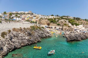 Een kustplaats met rotsachtige oevers, helder turquoise water en gebouwen in mediterrane stijl.