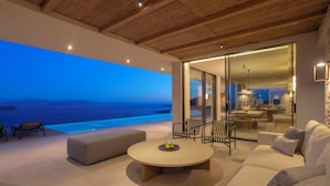 A modern living room with a large window overlooking a pool and the sea. There is a round coffee table and a sofa with cushions. - Oikos Nostos - Three Bedroom Villa, Sleeps 6 (Lefkada City)